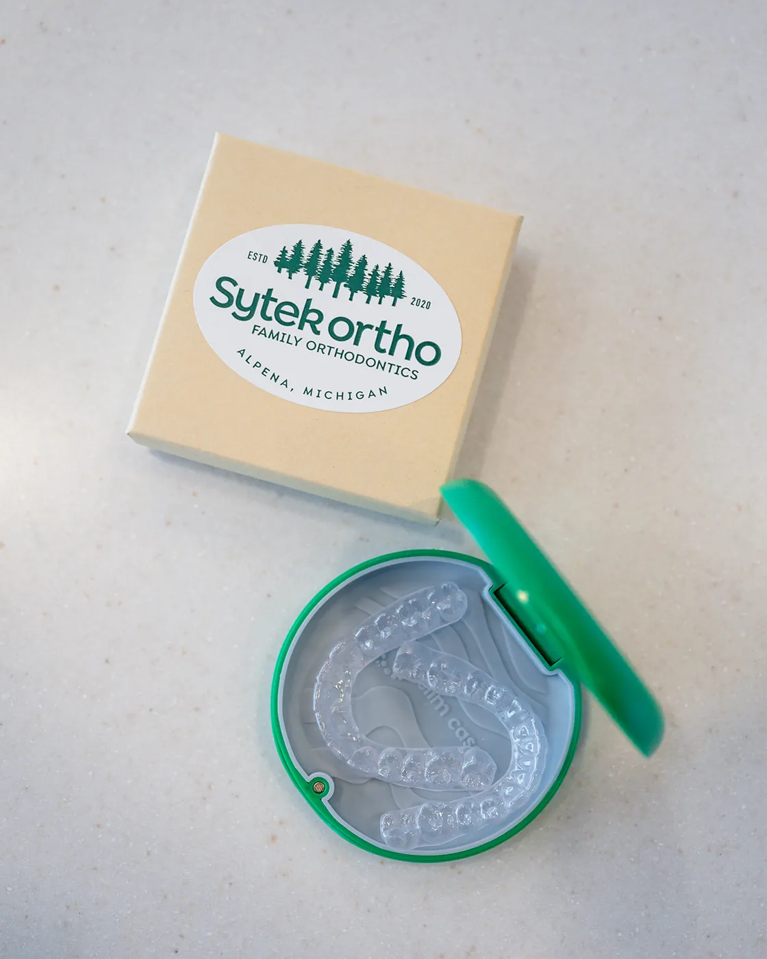 Clear retainers in an open green case beside a branded Sytek Ortho box.